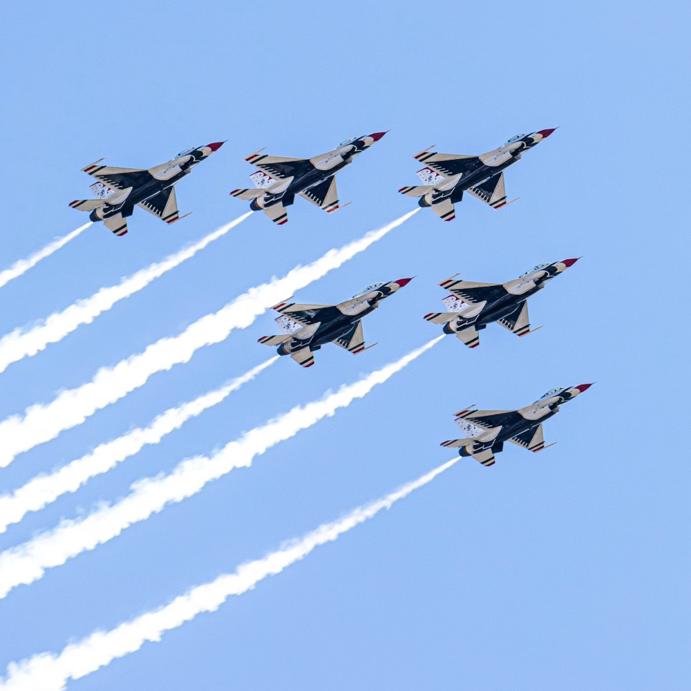 A six-aircraft formation climbing in close order, each jet trailing a white smoke line