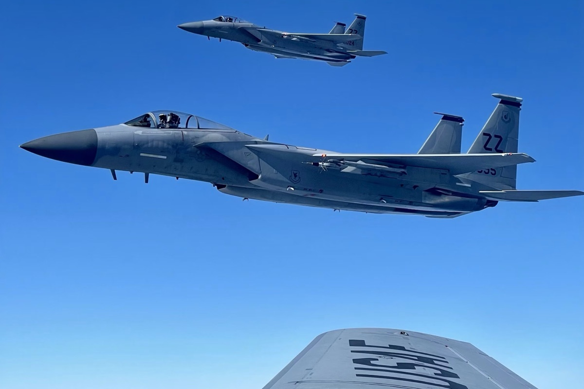 Two fighter aircraft in level flight above the wing of a larger aircraft at high altitude