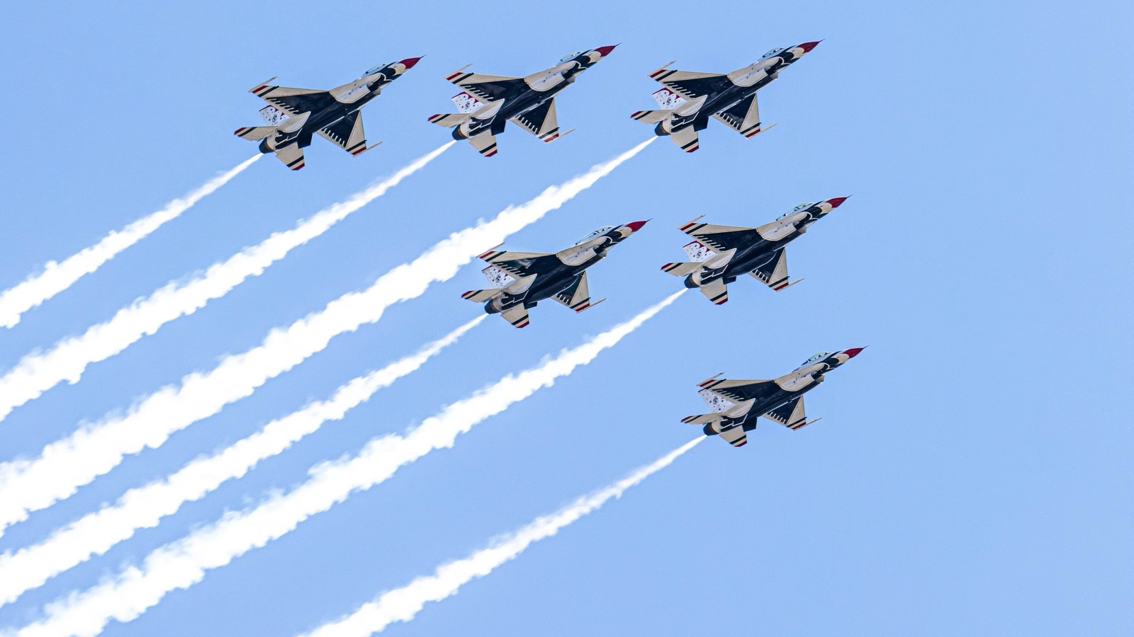 A formation of six aircraft holding precise spacing while trailing parallel smoke lines